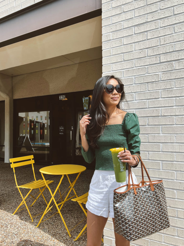 Blogger Hoang-Kim wearing a green smocked top with white linen shorts carrying a Goyard St Louis PM tote with a Junbi milky matcha.