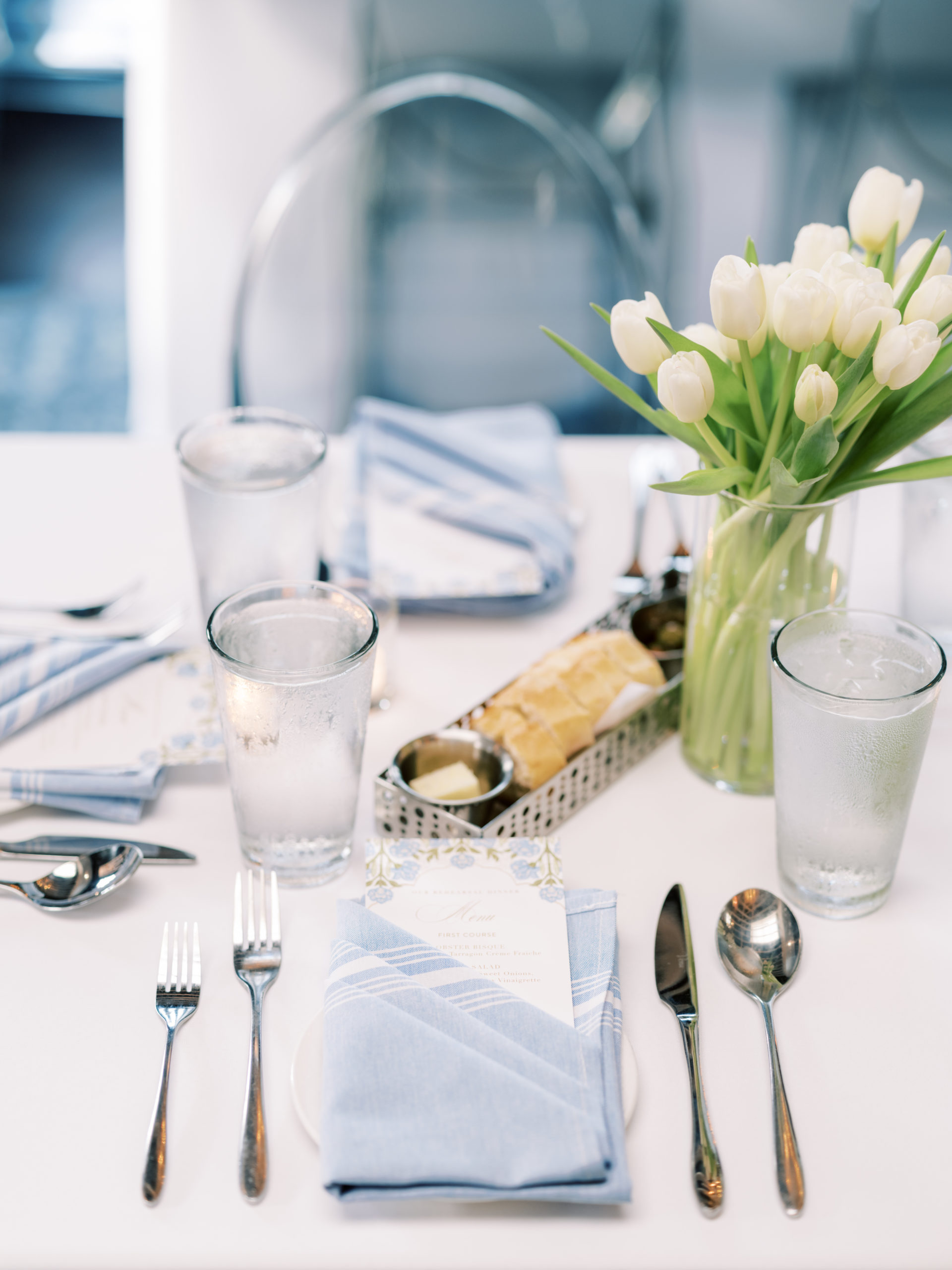 Light blue rehearsal dinner table setting with light blue linens, white tulips and blue floral menus from the knot