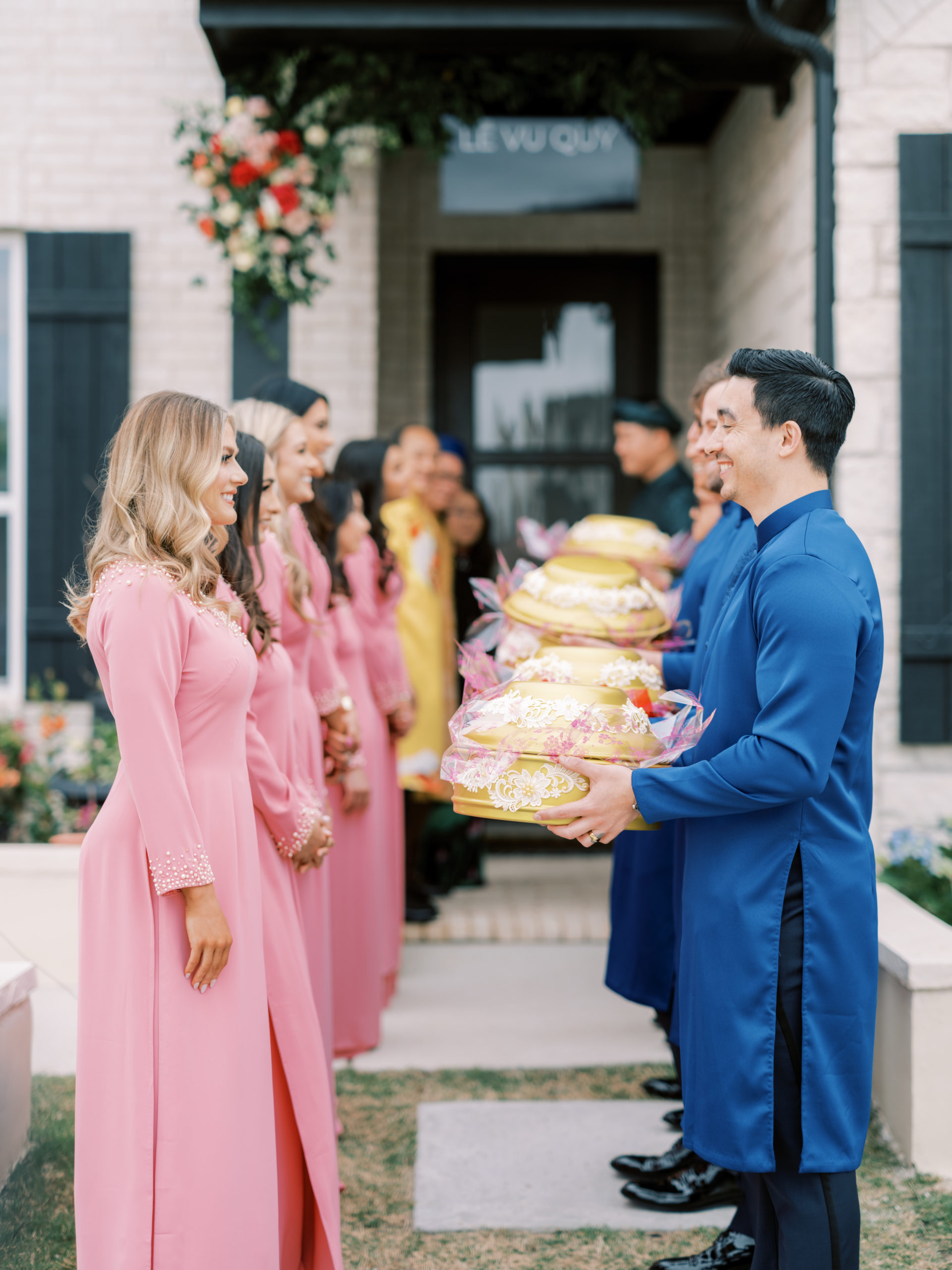 Sarah Rose Summers (birdesmaid) and Sebastian Ornstein (groomsman) exchange gifts on behalf of the groom and bride's family during a Vietnamese wedding ceremony wearing ao dai.