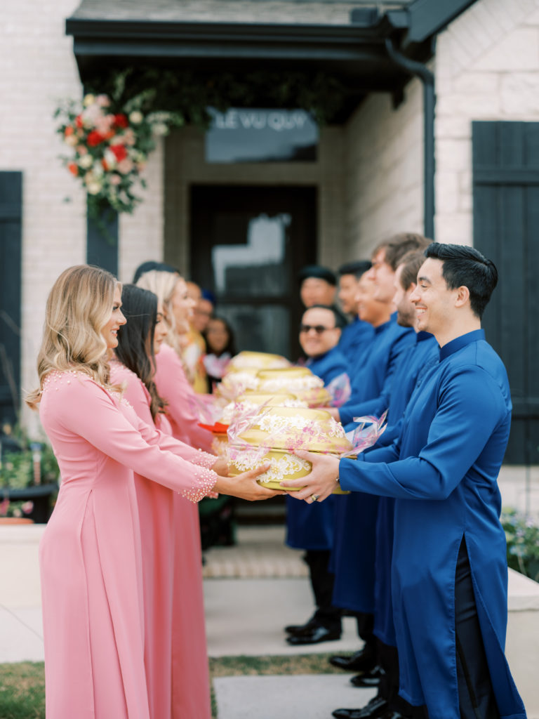 Sarah Rose Summers (birdesmaid) and Sebastian Ornstein (groomsman) exchange gifts on behalf of the groom and bride's family during a Vietnamese wedding ceremony wearing ao dai.