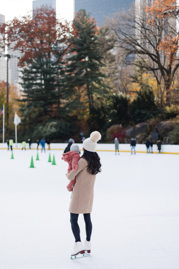 Hoang-Kim Cung holding her baby girl wearing a Carter's bear bunting suit with a jcrew cashmere beanie ice skating at Wollman Rink in New York City