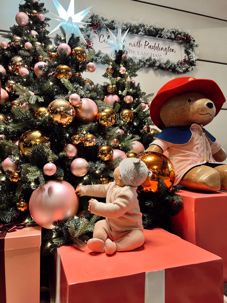 Baby wearing La Coqueta merino wool pink stripe set with the Paddington Bear display at the Langham New York hotel