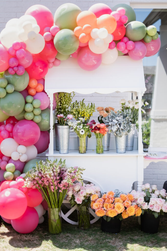 Make your own floral arrangement cart at a floral first birthday party with flowers from Something Pretty Floral on a white cart with green, pink, orange and cream balloons