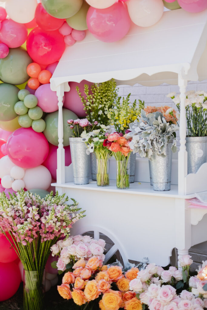 Make your own floral arrangement cart at a floral first birthday party with flowers from Something Pretty Floral on a white cart with green, pink, orange and cream balloons