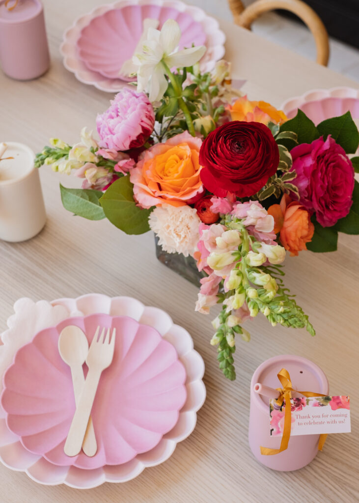 kids birthday party table setup for a floral first birthday with pink scalloped plates from meri meri, silicone straw cups as party favors and floral centerpieces