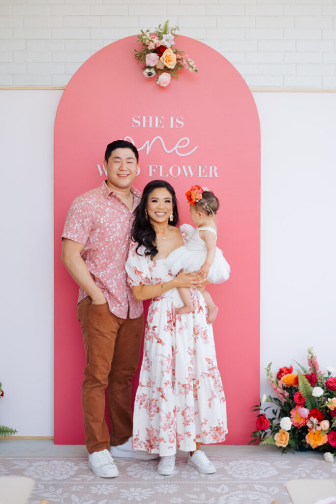 Blogger, Hoang-Kim, her husband and daughter in front of a floral first birthday party backdrop