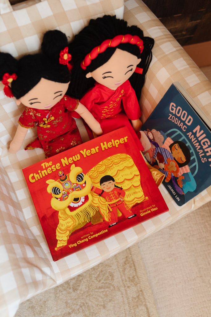 Asian cultural dolls holding a Chinese New Year Helper book on a gingham Nestig mini chair for toddlers.